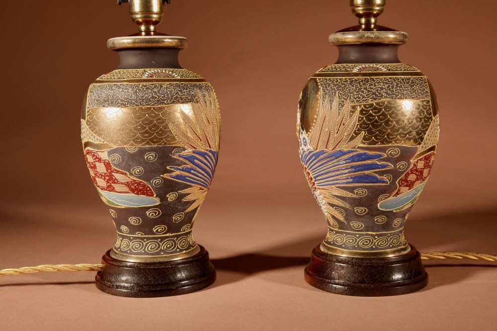 A pair of small Japanese Satsuma ceramic table lamps featuring figure paintings, gold gilding, dark wooden bases, and pleated cream shades. View IX