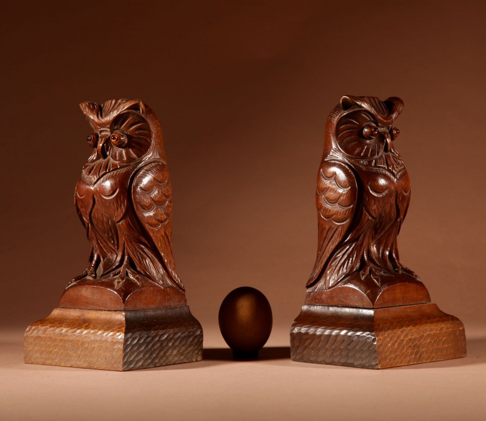 A pair of hand-carved dark wood owl figures with glass eyes mounted on carved wooden bases.