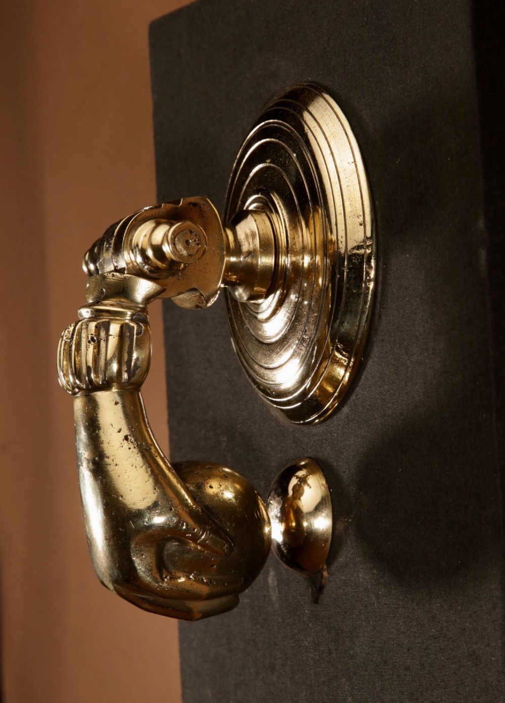 A cast bronze door knocker shaped as a hand holding a sphere, fitted to a circular stepped backplate.