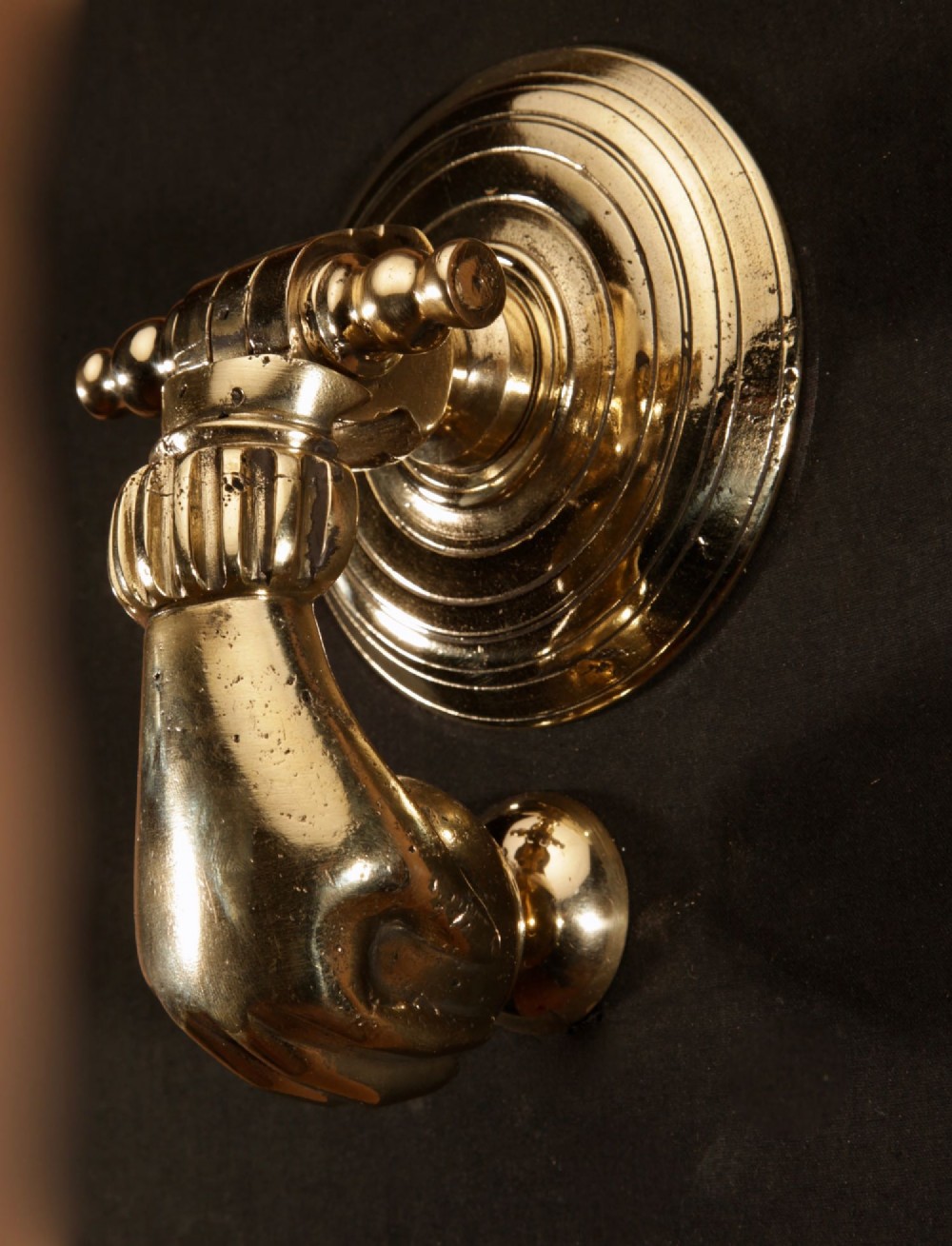 A cast bronze door knocker shaped as a hand holding a sphere, fitted to a circular stepped backplate. View II