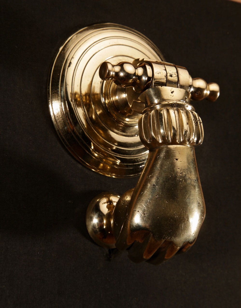 A cast bronze door knocker shaped as a hand holding a sphere, fitted to a circular stepped backplate. View III