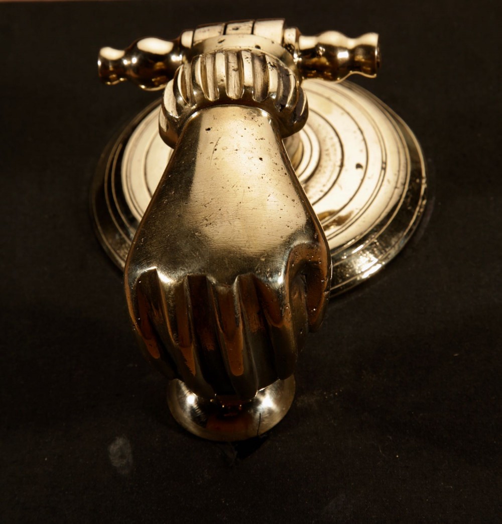 A cast bronze door knocker shaped as a hand holding a sphere, fitted to a circular stepped backplate. View IV