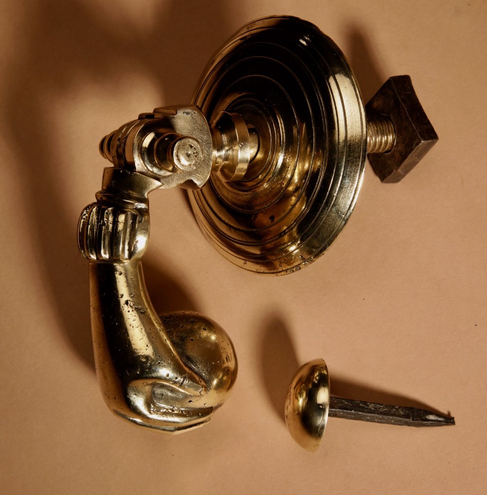 A cast bronze door knocker shaped as a hand holding a sphere, fitted to a circular stepped backplate. View VI