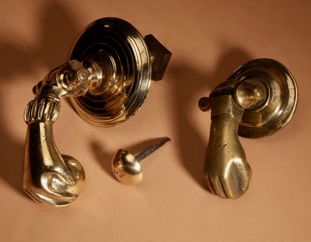 A cast bronze door knocker shaped as a hand holding a sphere, fitted to a circular stepped backplate. View X
