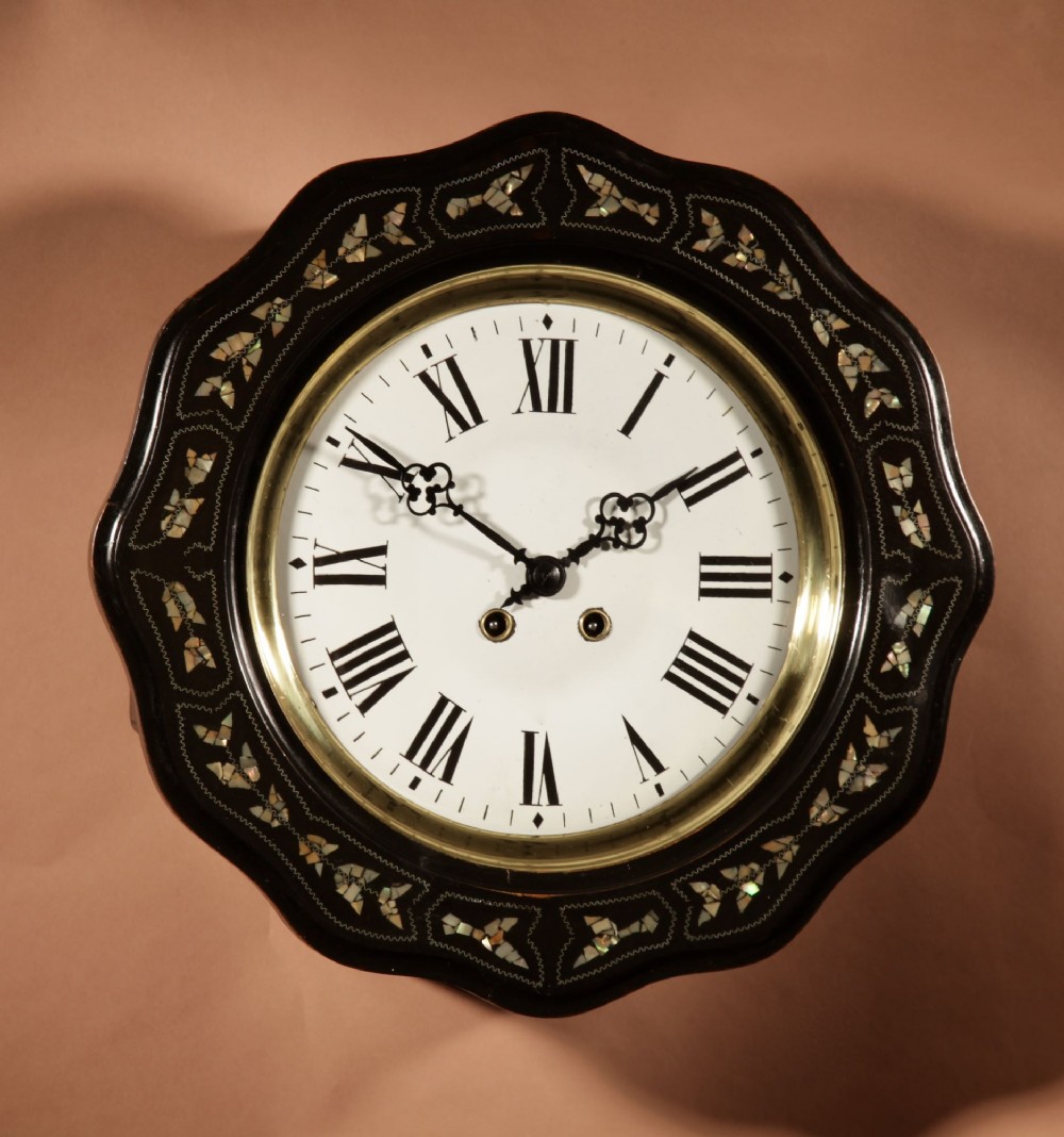 An ebonised French wall clock featuring a scalloped outer frame with floral mother-of-pearl inlay, a brass bezel, and a white dial with black Roman numerals. View II