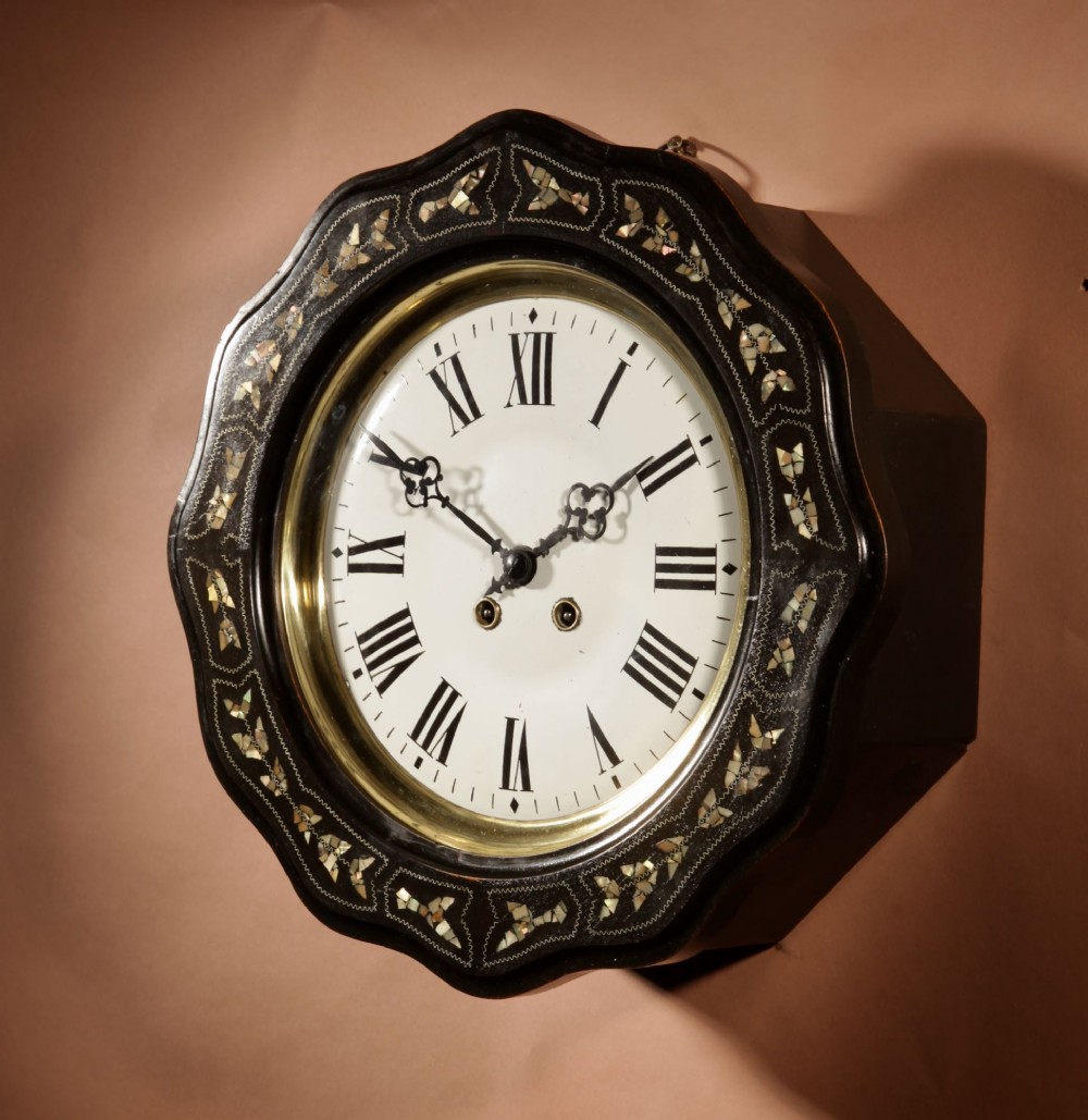 An ebonised French wall clock featuring a scalloped outer frame with floral mother-of-pearl inlay, a brass bezel, and a white dial with black Roman numerals. View III