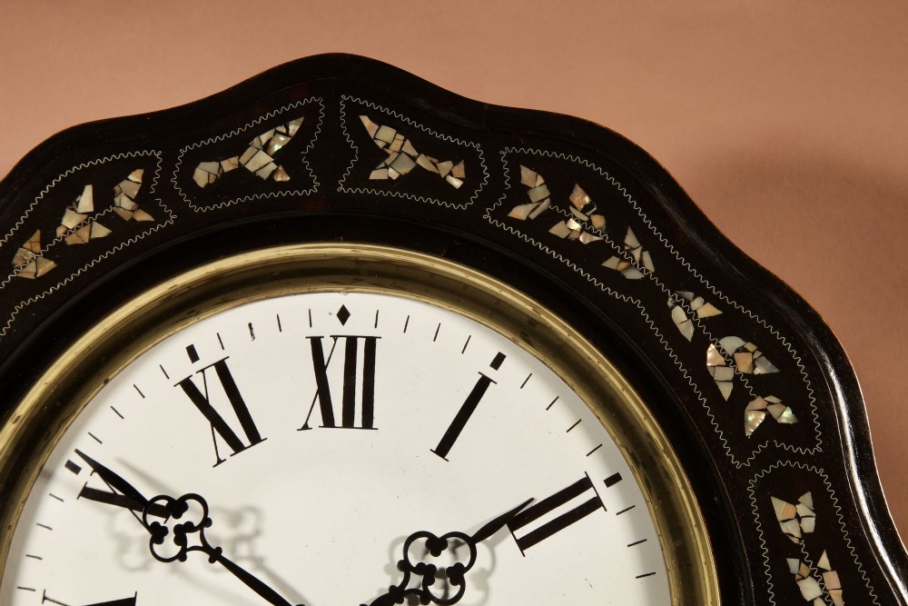 An ebonised French wall clock featuring a scalloped outer frame with floral mother-of-pearl inlay, a brass bezel, and a white dial with black Roman numerals. View IV