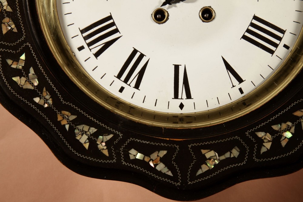 An ebonised French wall clock featuring a scalloped outer frame with floral mother-of-pearl inlay, a brass bezel, and a white dial with black Roman numerals. View V