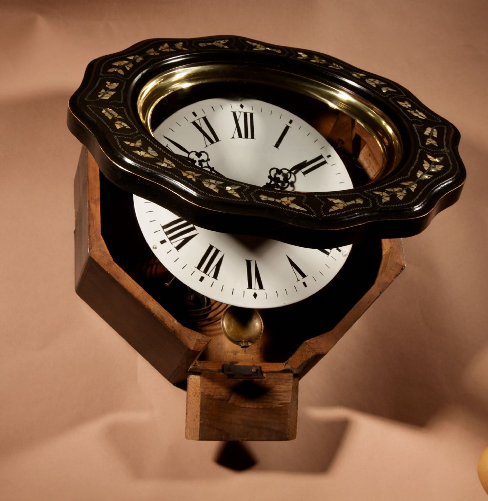An ebonised French wall clock featuring a scalloped outer frame with floral mother-of-pearl inlay, a brass bezel, and a white dial with black Roman numerals. View VI