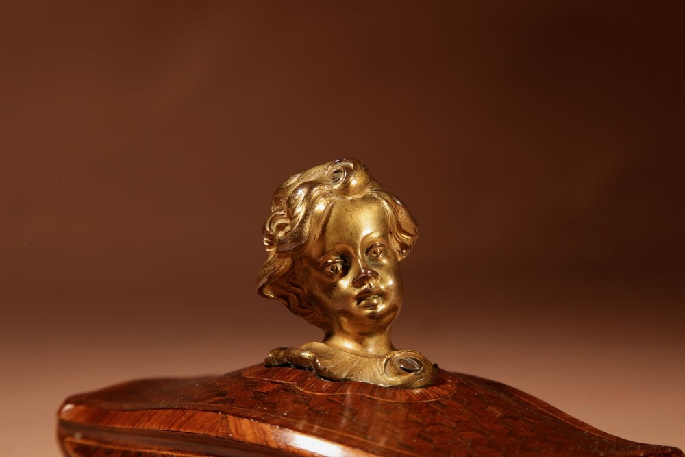 A nineteenth-century French rocker blotter featuring geometric wood parquetry inlay, a green felt underside, and a sculpted gilt bronze cherub head handle. View V