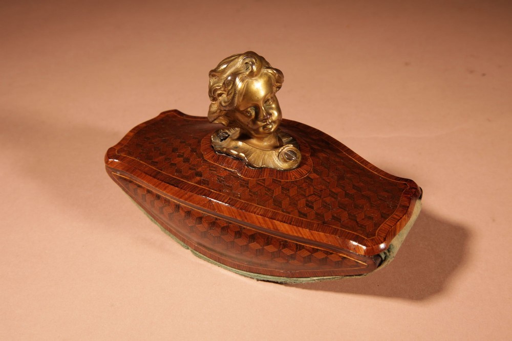 A nineteenth-century French rocker blotter featuring geometric wood parquetry inlay, a green felt underside, and a sculpted gilt bronze cherub head handle. View IX