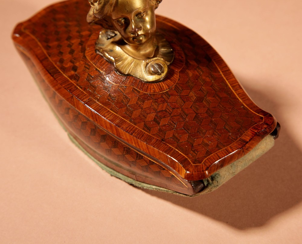 A nineteenth-century French rocker blotter featuring geometric wood parquetry inlay, a green felt underside, and a sculpted gilt bronze cherub head handle. View XV