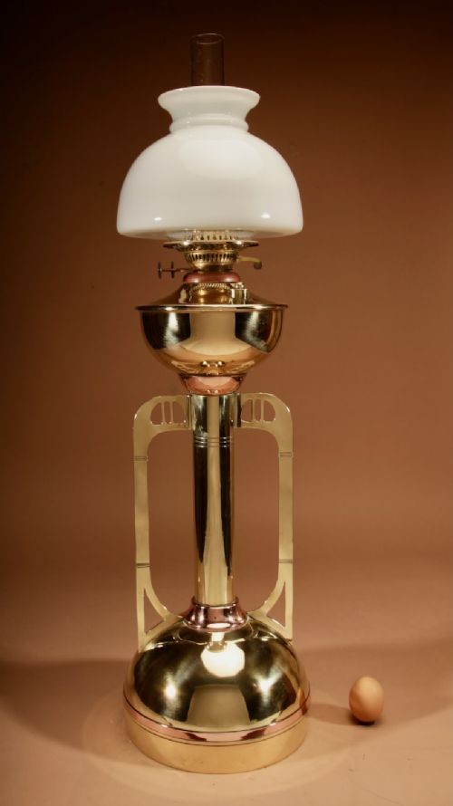 An antique Secessionist brass and copper paraffin table lamp featuring a white glass shade, central column body, and geometric side handles.