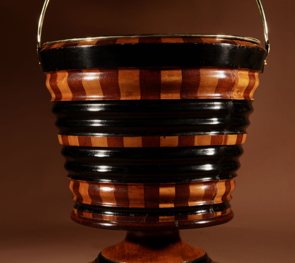 A Dutch coopered wooden peat bucket with alternating brown and ebonised staves, a brass swing handle, and a removable metal liner on a footed pedestal base. View II