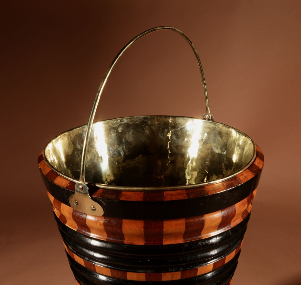 A Dutch coopered wooden peat bucket with alternating brown and ebonised staves, a brass swing handle, and a removable metal liner on a footed pedestal base. View V