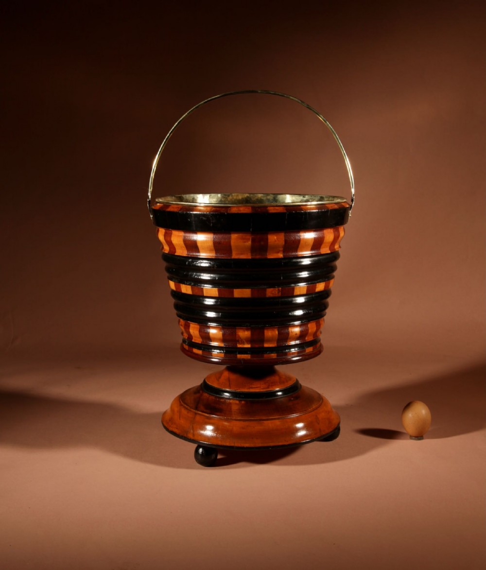 A Dutch coopered wooden peat bucket with alternating brown and ebonised staves, a brass swing handle, and a removable metal liner on a footed pedestal base. View VII
