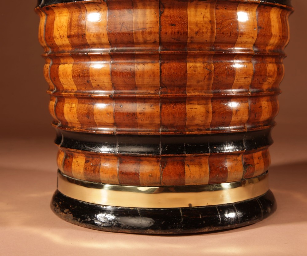 An antique coopered wooden peat bucket featuring alternating light and dark ribbed wood staves, ebonised bands, a brass rim, and a brass swing handle. View IV