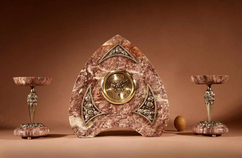A three-piece French Art Deco clock garniture crafted from veined rose marble with brass floral embellishments and matching side tazzas.