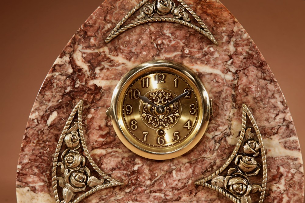A three-piece French Art Deco clock garniture crafted from veined rose marble with brass floral embellishments and matching side tazzas. View II