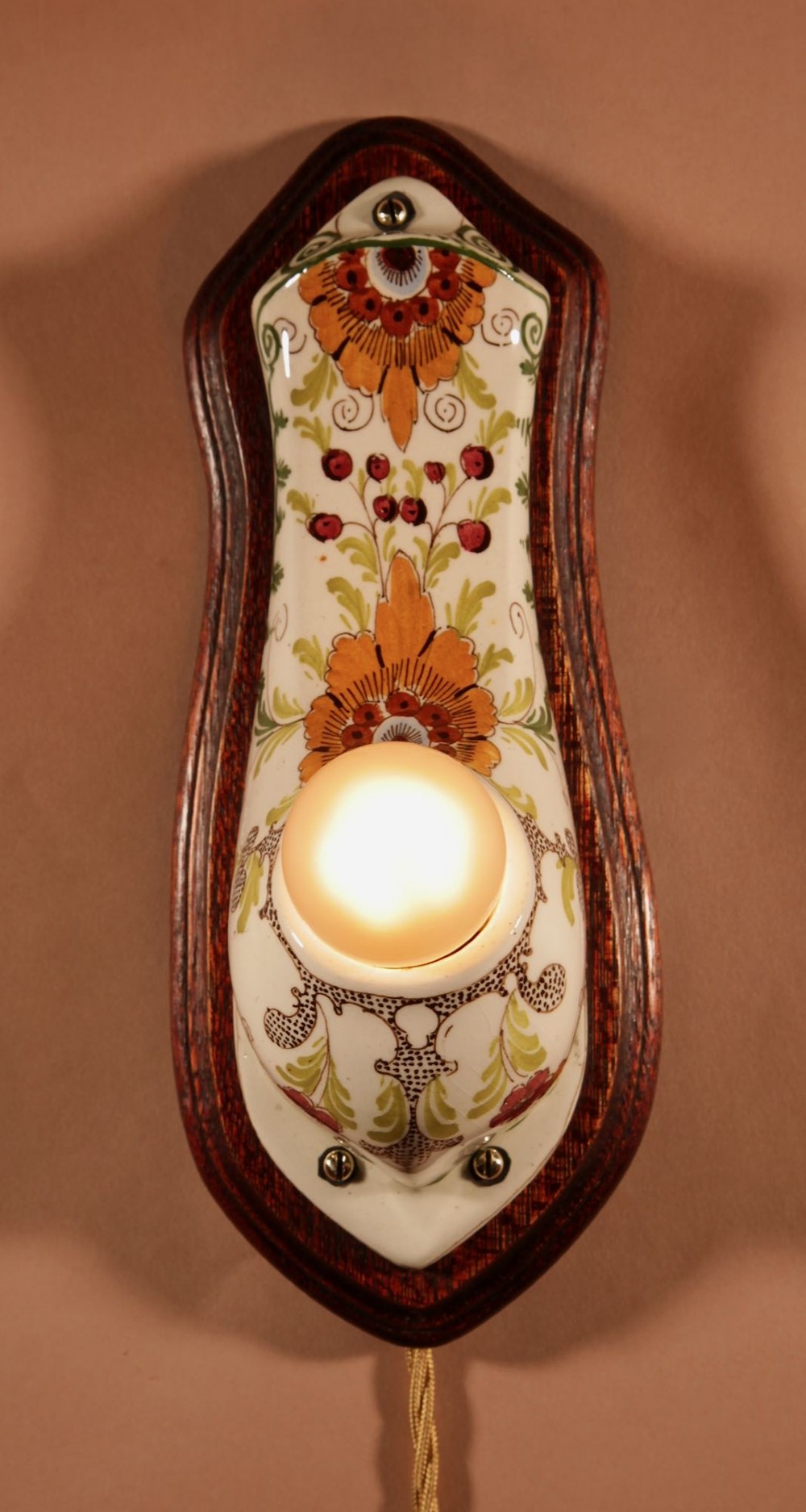 A Dutch Art Nouveau hand-painted ceramic wall sconce with floral patterns, mounted on a dark wooden backplate with an illuminated bulb. View IV