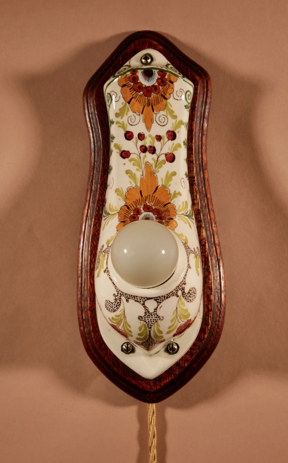 A Dutch Art Nouveau hand-painted ceramic wall sconce with floral patterns, mounted on a dark wooden backplate with an illuminated bulb. View V