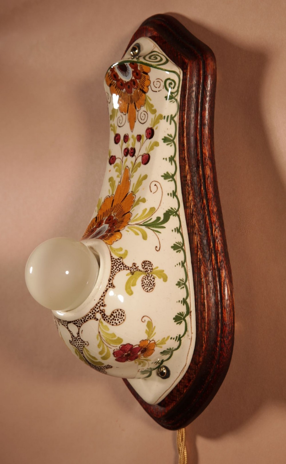 A Dutch Art Nouveau hand-painted ceramic wall sconce with floral patterns, mounted on a dark wooden backplate with an illuminated bulb. View VI