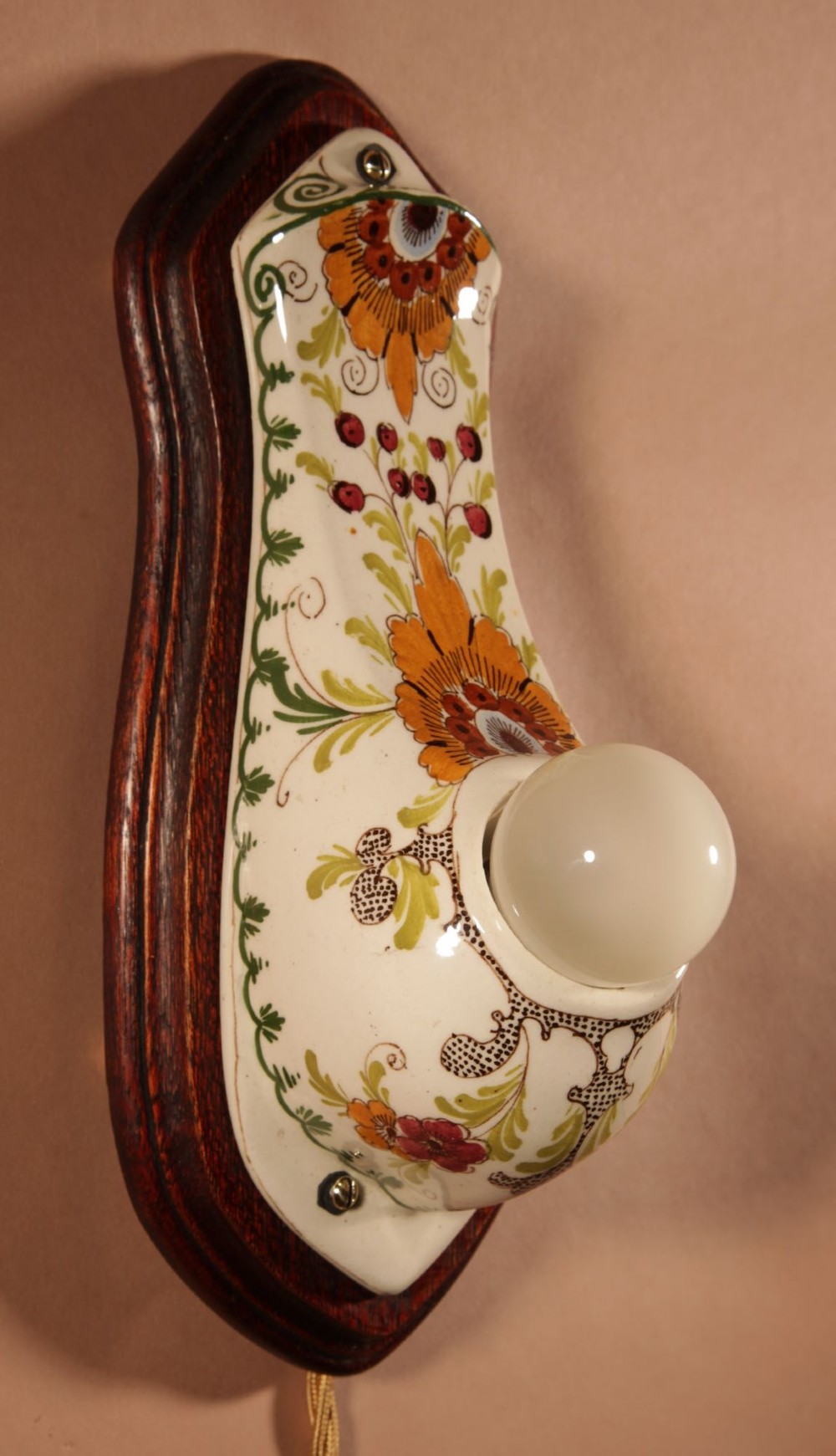 A Dutch Art Nouveau hand-painted ceramic wall sconce with floral patterns, mounted on a dark wooden backplate with an illuminated bulb. View VII