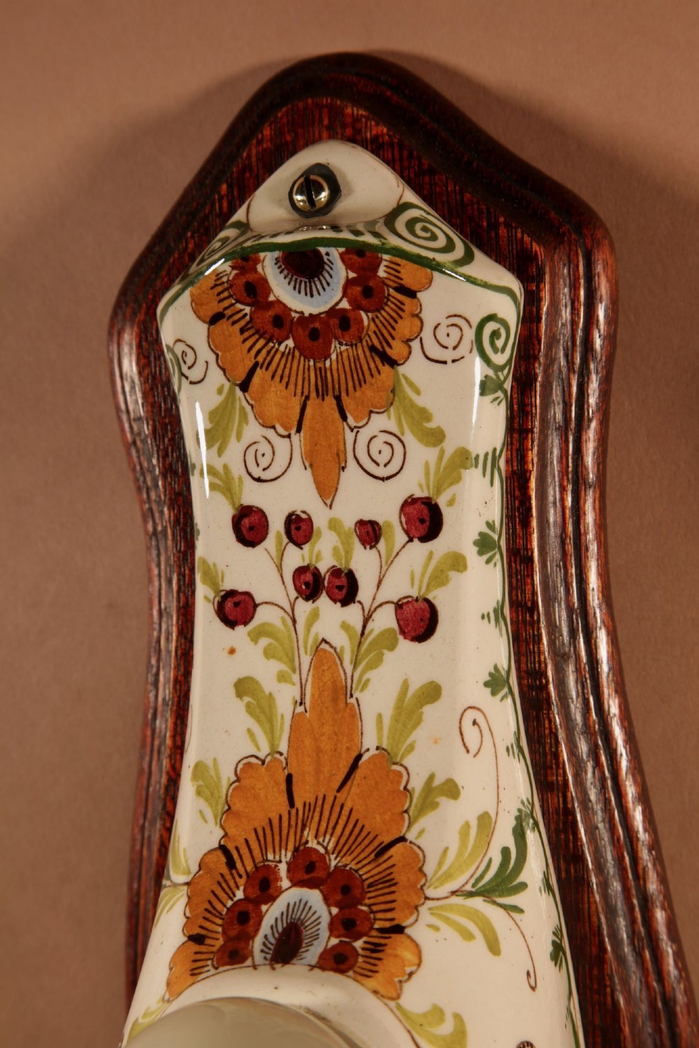 A Dutch Art Nouveau hand-painted ceramic wall sconce with floral patterns, mounted on a dark wooden backplate with an illuminated bulb. View VIII