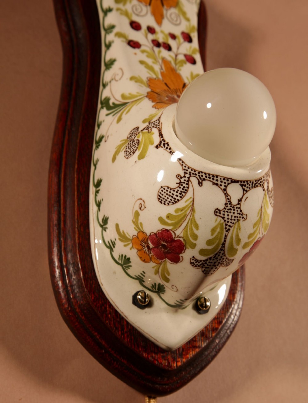 A Dutch Art Nouveau hand-painted ceramic wall sconce with floral patterns, mounted on a dark wooden backplate with an illuminated bulb. View X