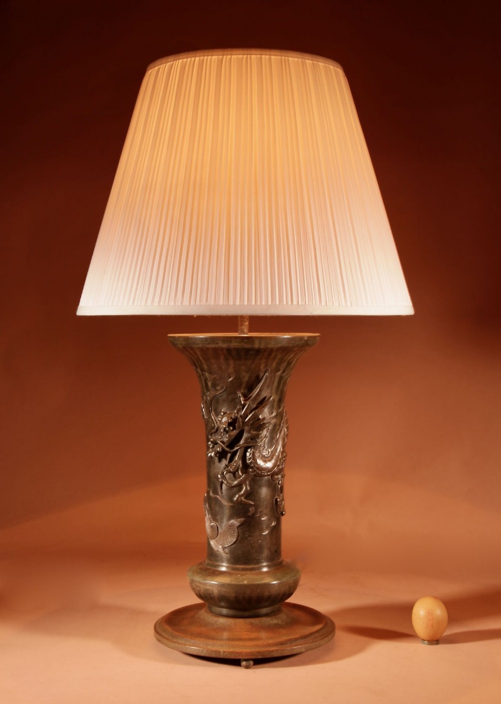A dark patinated Japanese bronze table lamp featuring a relief-carved dragon wrapped around the central column, topped with a cream pleated lampshade.