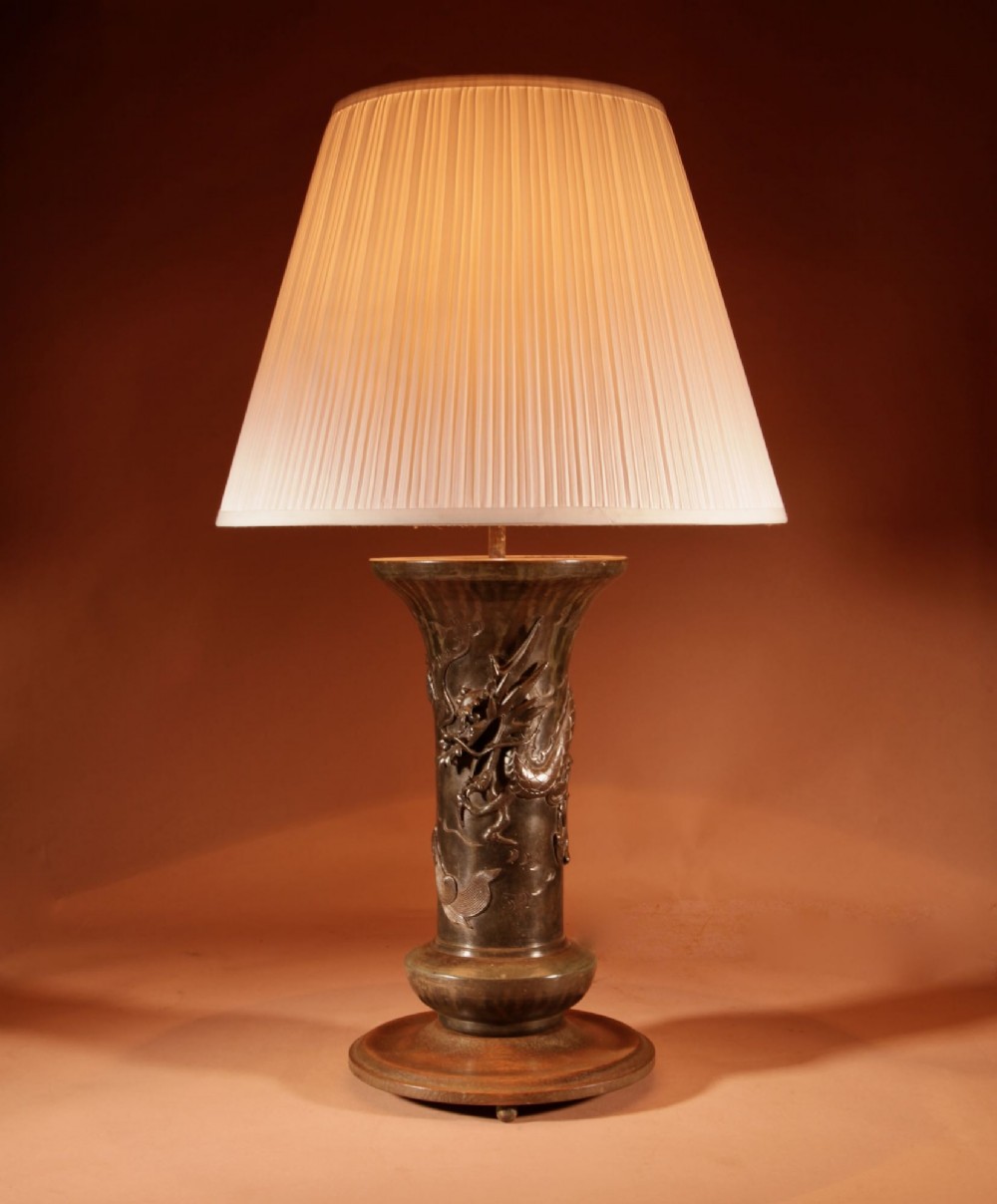 A dark patinated Japanese bronze table lamp featuring a relief-carved dragon wrapped around the central column, topped with a cream pleated lampshade. View II