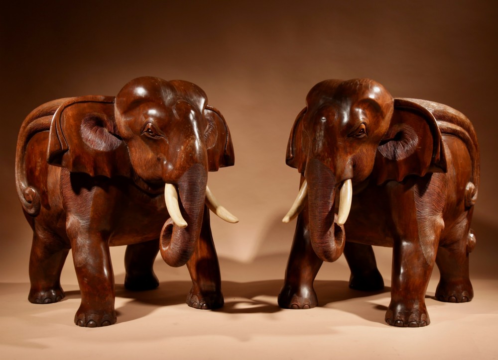 A pair of heavy hand-carved wooden armchairs sculpted in the form of standing elephants with textured hides and light-coloured tusks. View II