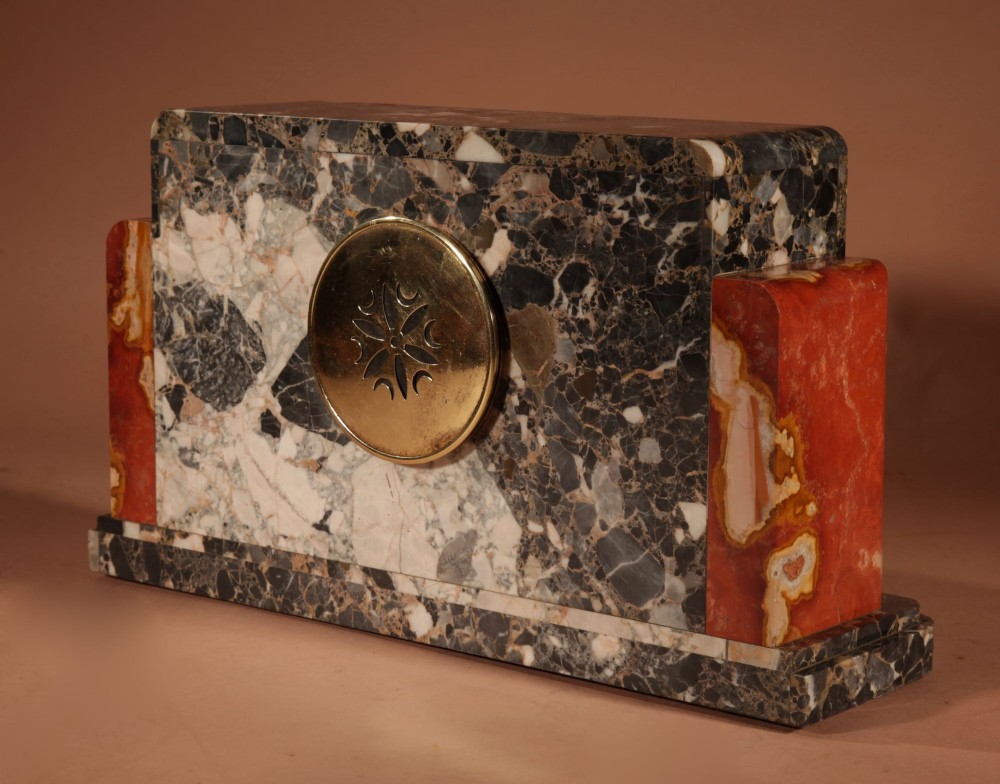 An Art Deco clock garniture set constructed from dark speckled stone and coral marble featuring a central rectangular clock with gilt numerals and two matching side pieces. View VI