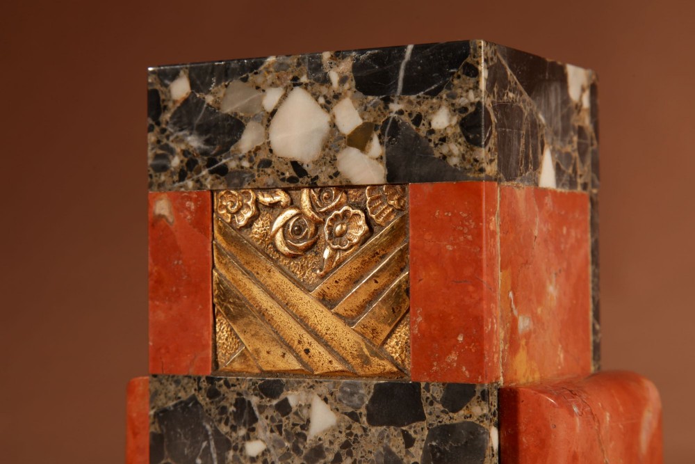 An Art Deco clock garniture set constructed from dark speckled stone and coral marble featuring a central rectangular clock with gilt numerals and two matching side pieces. View X