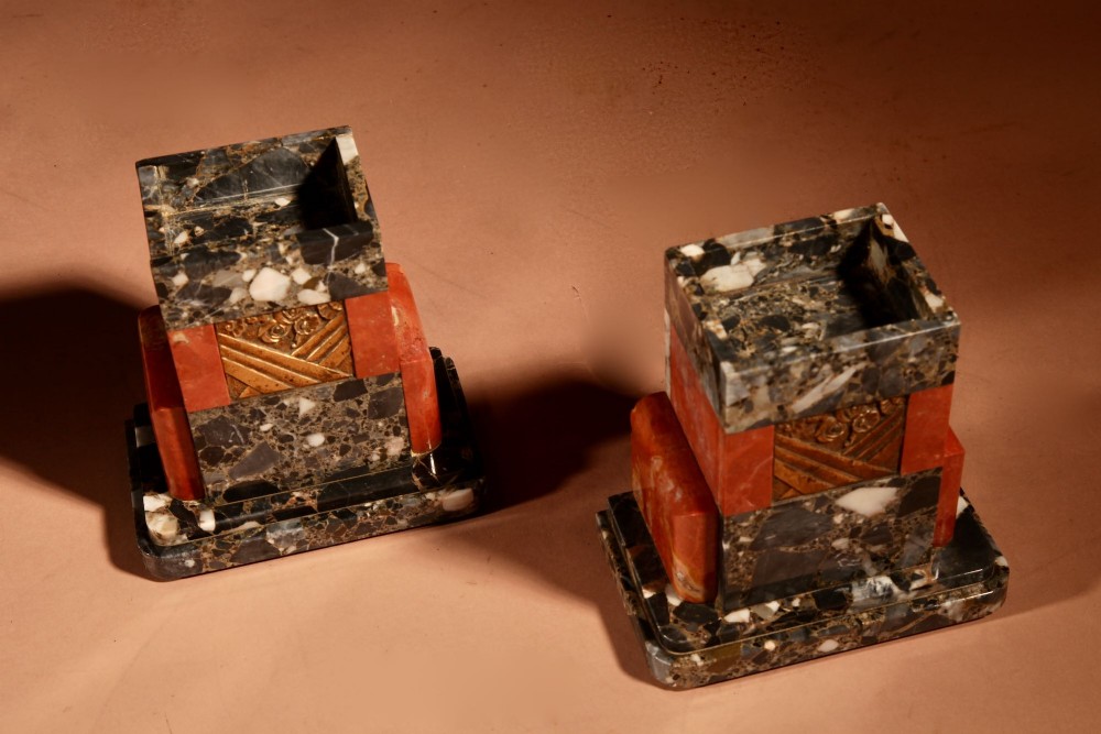 An Art Deco clock garniture set constructed from dark speckled stone and coral marble featuring a central rectangular clock with gilt numerals and two matching side pieces. View XII