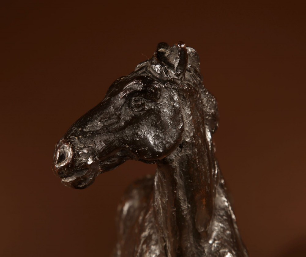 A dark patinated bronze sculpture of a muscular draft horse with one raised foreleg mounted on a rectangular stone base. View IV