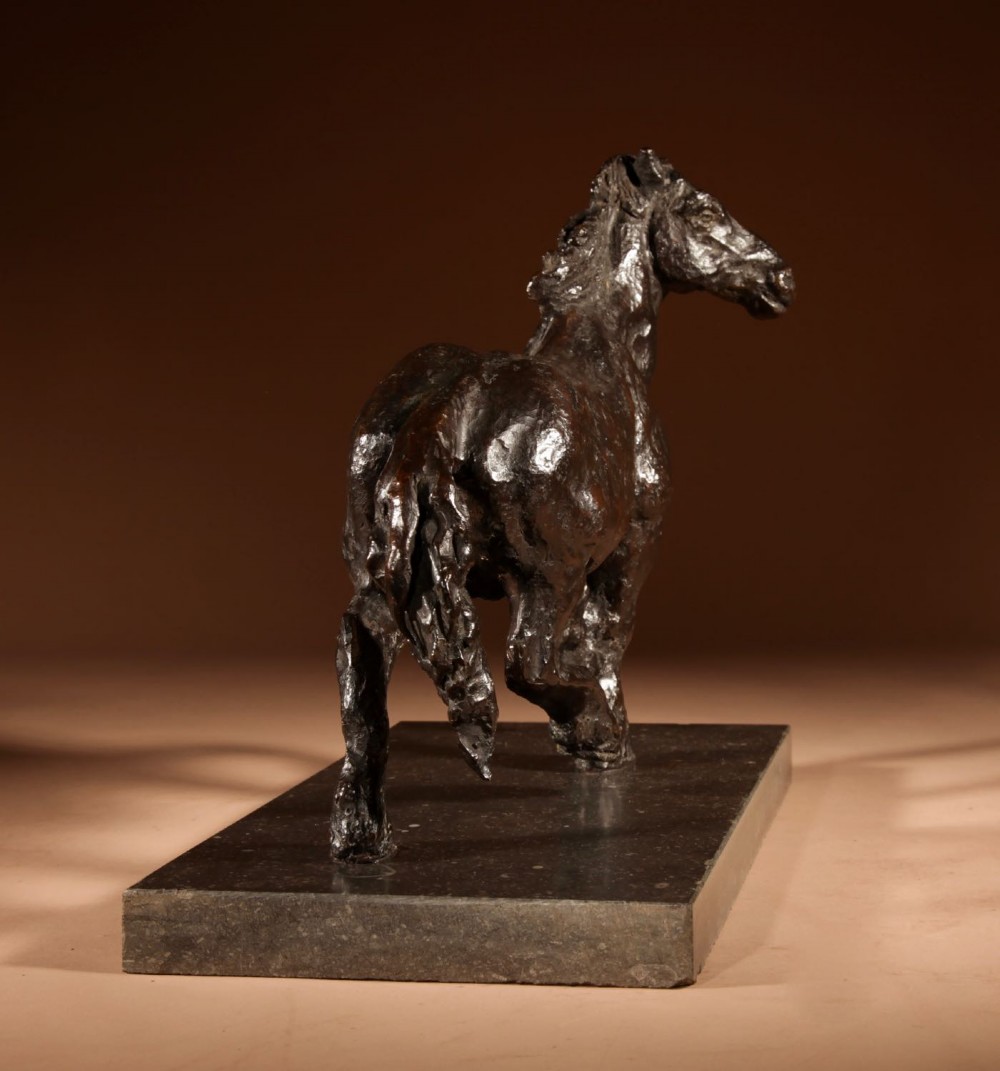 A dark patinated bronze sculpture of a muscular draft horse with one raised foreleg mounted on a rectangular stone base. View VIII