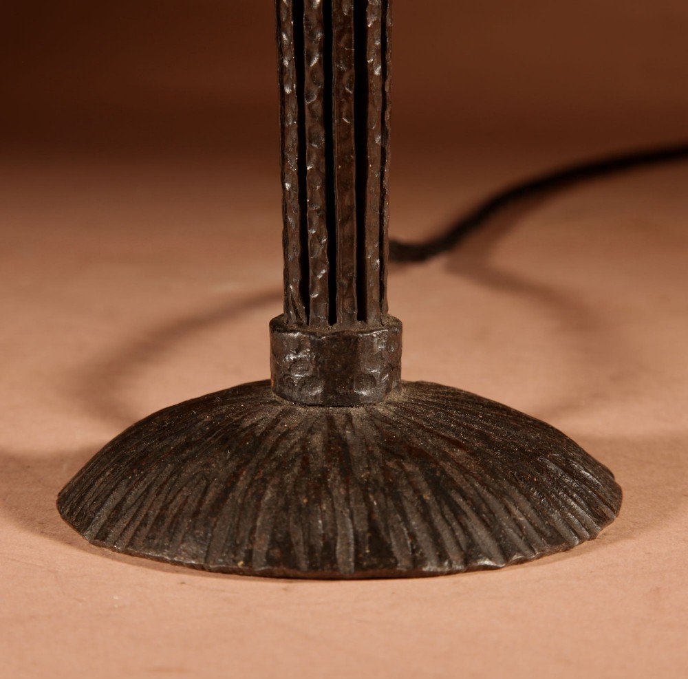 An illuminated French Art Deco table lamp with a flared opalescent glass shade set atop a dark, hammered wrought iron stem and circular base. View III