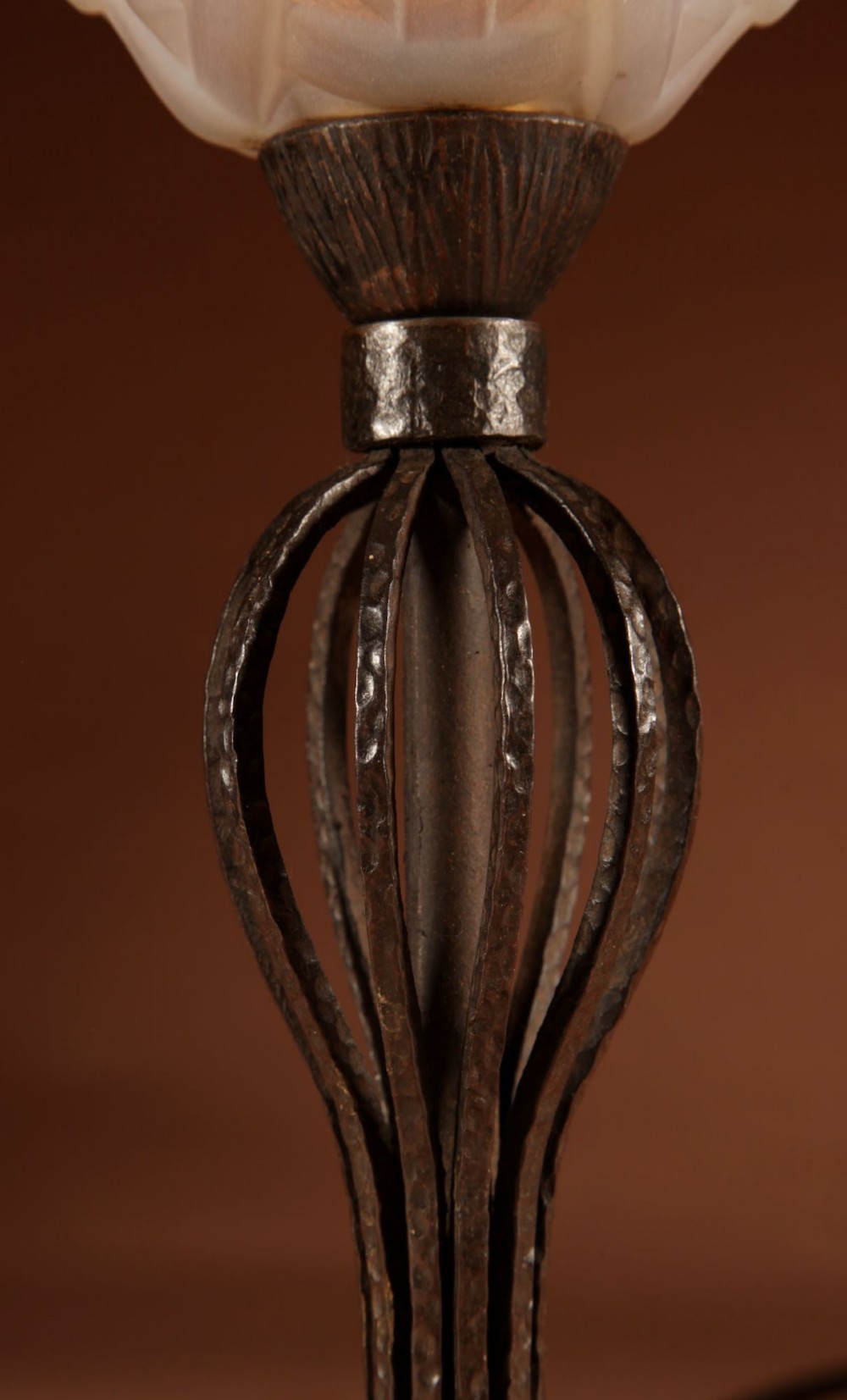 An illuminated French Art Deco table lamp with a flared opalescent glass shade set atop a dark, hammered wrought iron stem and circular base. View IV