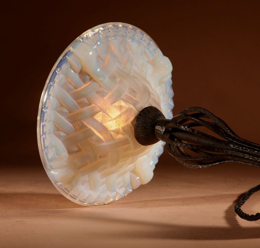 An illuminated French Art Deco table lamp with a flared opalescent glass shade set atop a dark, hammered wrought iron stem and circular base. View VI