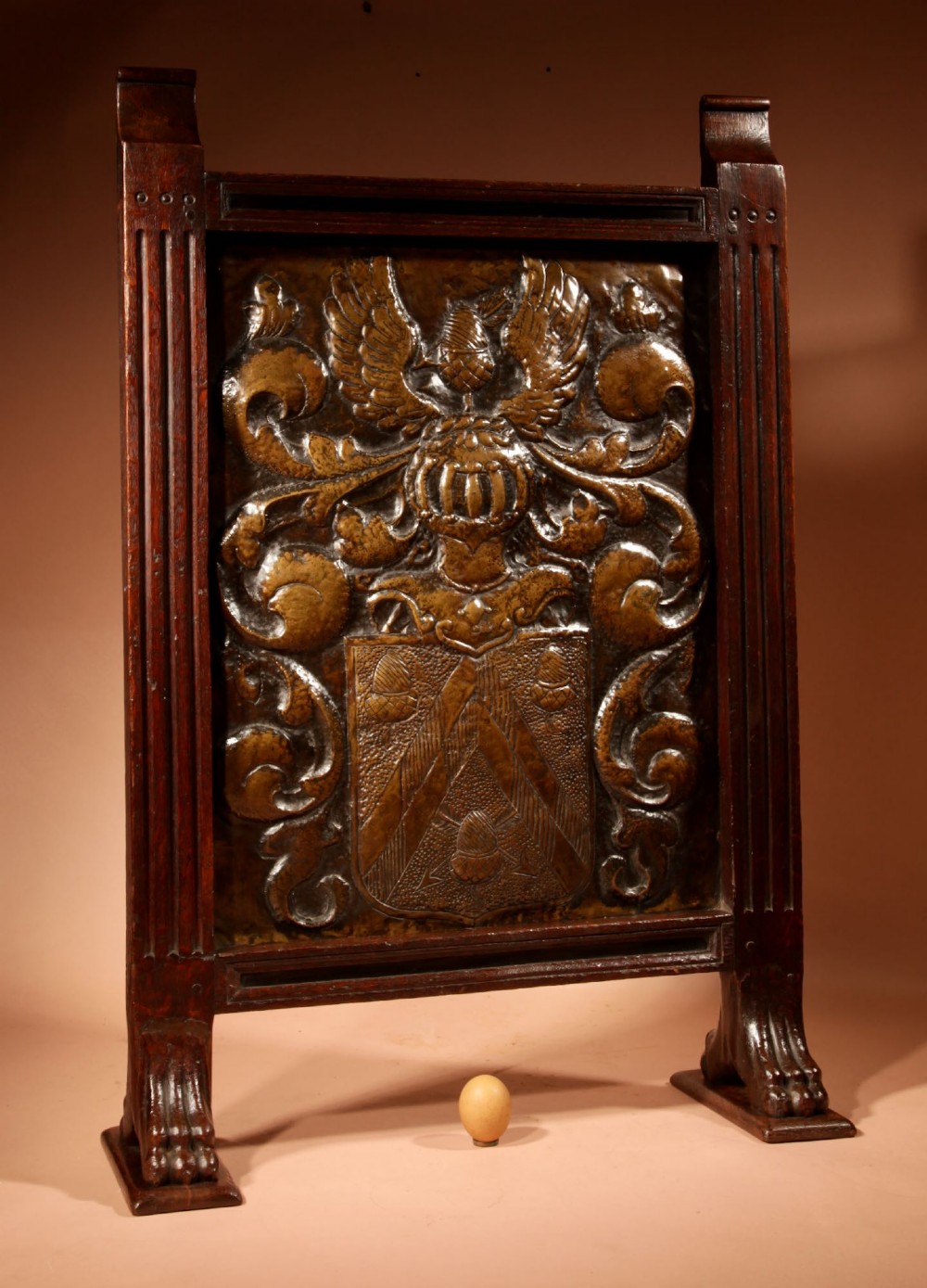An antique dark oak fire screen featuring a central chased brass panel depicting a coat of arms with an eagle and acorns. View II