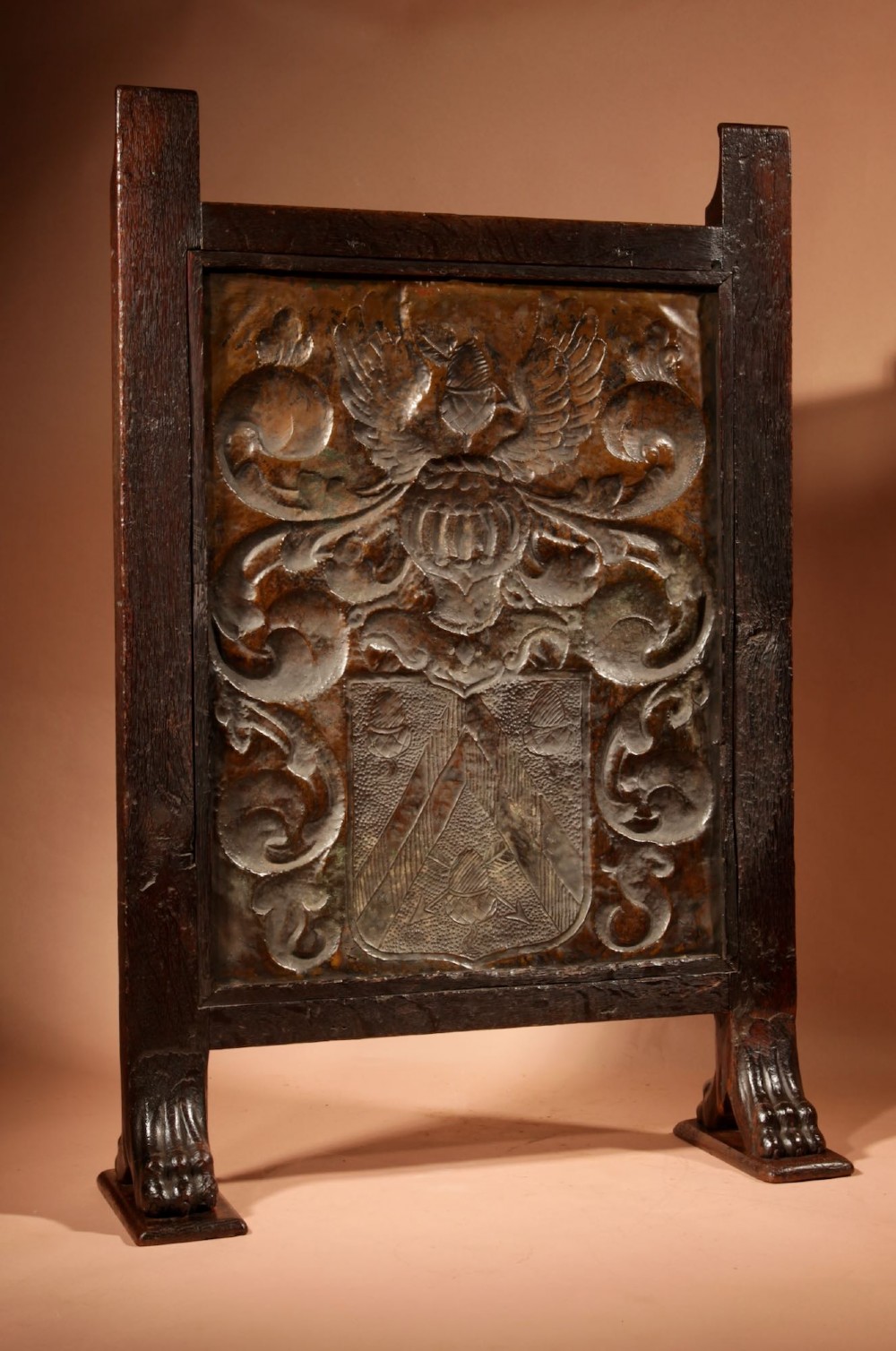 An antique dark oak fire screen featuring a central chased brass panel depicting a coat of arms with an eagle and acorns. View IX