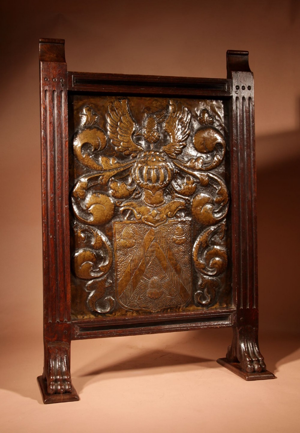 An antique dark oak fire screen featuring a central chased brass panel depicting a coat of arms with an eagle and acorns. View XV