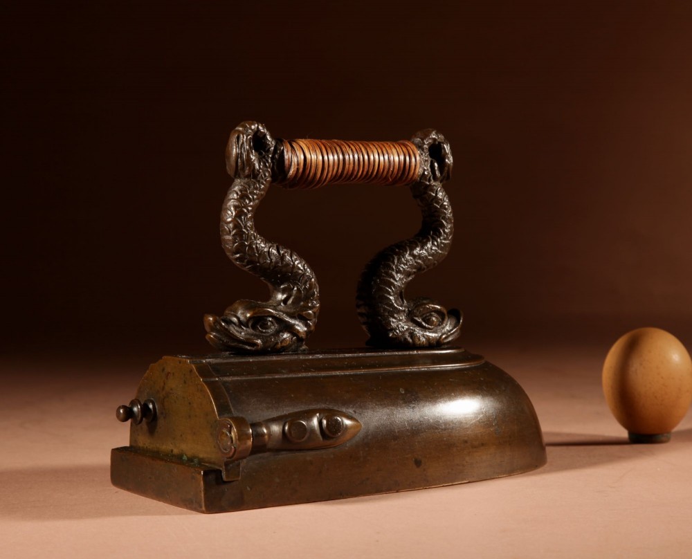 A nineteenth-century French bronze flat iron featuring twin dolphin-shaped supports, a cane-wrapped handle, and a rear door mechanism.