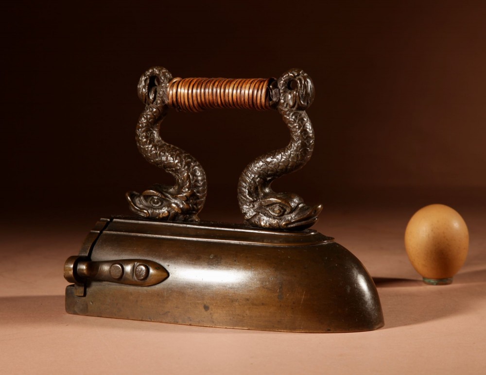 A nineteenth-century French bronze flat iron featuring twin dolphin-shaped supports, a cane-wrapped handle, and a rear door mechanism. View II