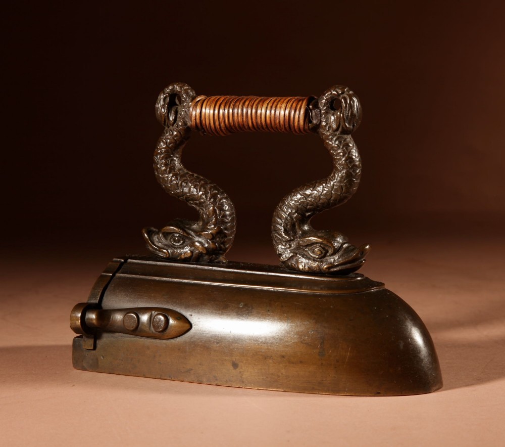 A nineteenth-century French bronze flat iron featuring twin dolphin-shaped supports, a cane-wrapped handle, and a rear door mechanism. View III
