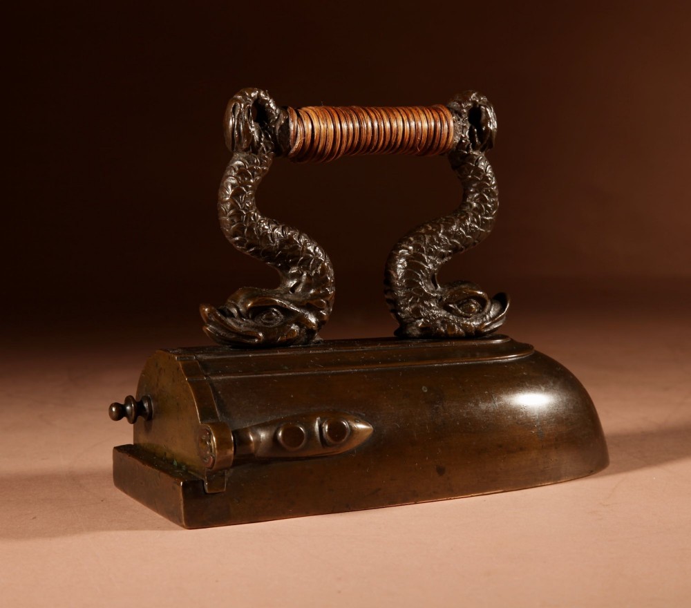 A nineteenth-century French bronze flat iron featuring twin dolphin-shaped supports, a cane-wrapped handle, and a rear door mechanism. View IV