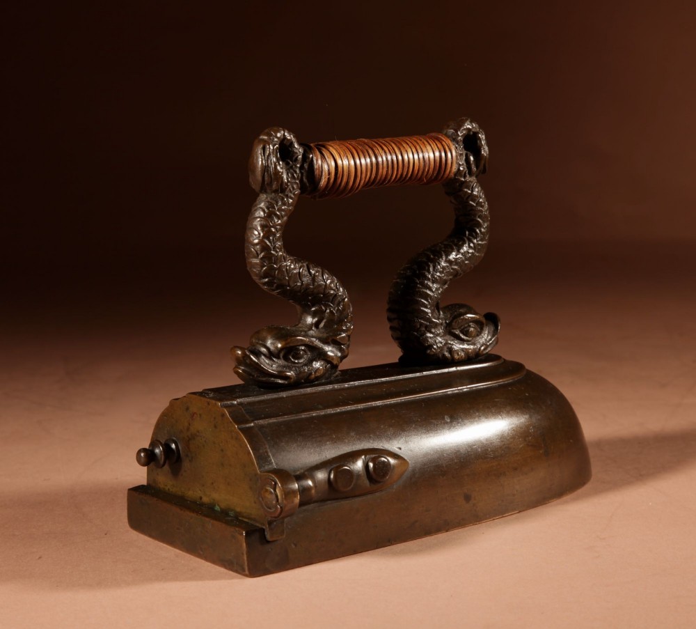 A nineteenth-century French bronze flat iron featuring twin dolphin-shaped supports, a cane-wrapped handle, and a rear door mechanism. View V