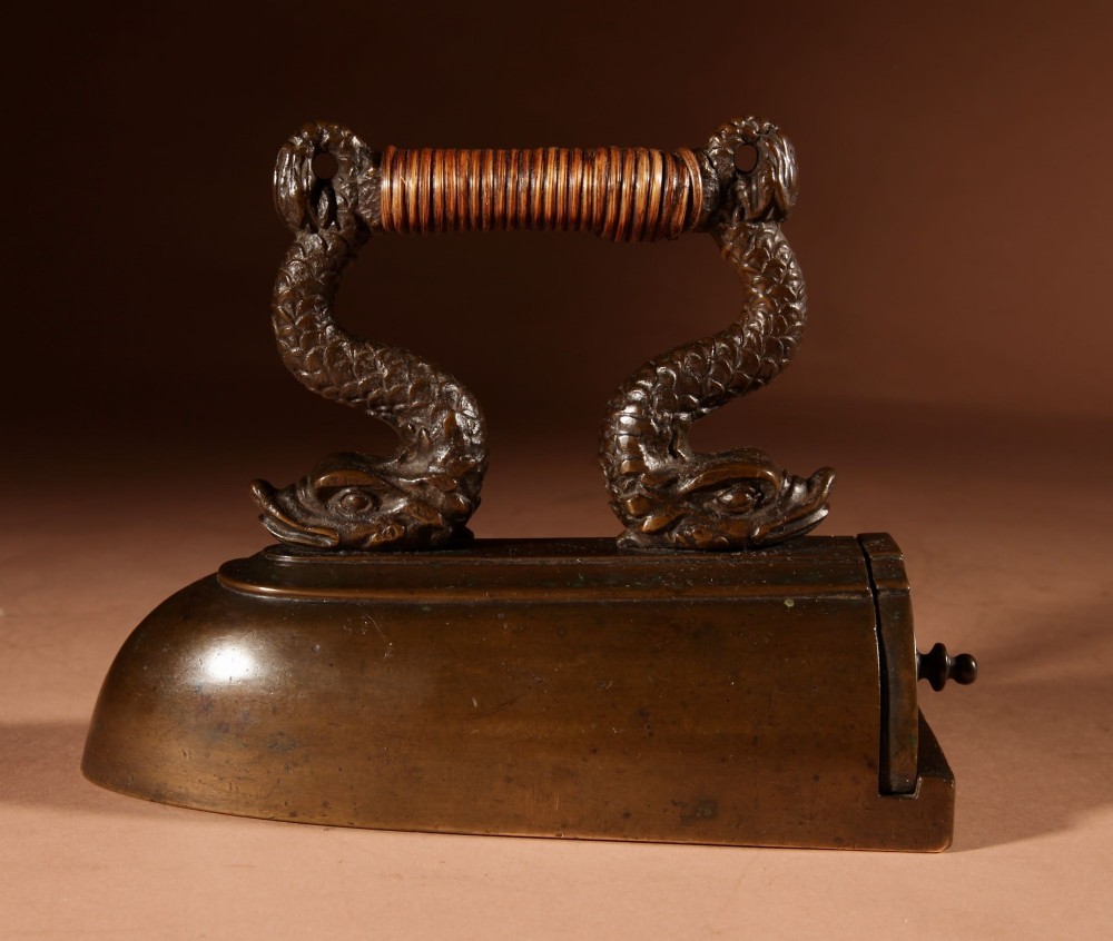 A nineteenth-century French bronze flat iron featuring twin dolphin-shaped supports, a cane-wrapped handle, and a rear door mechanism. View X