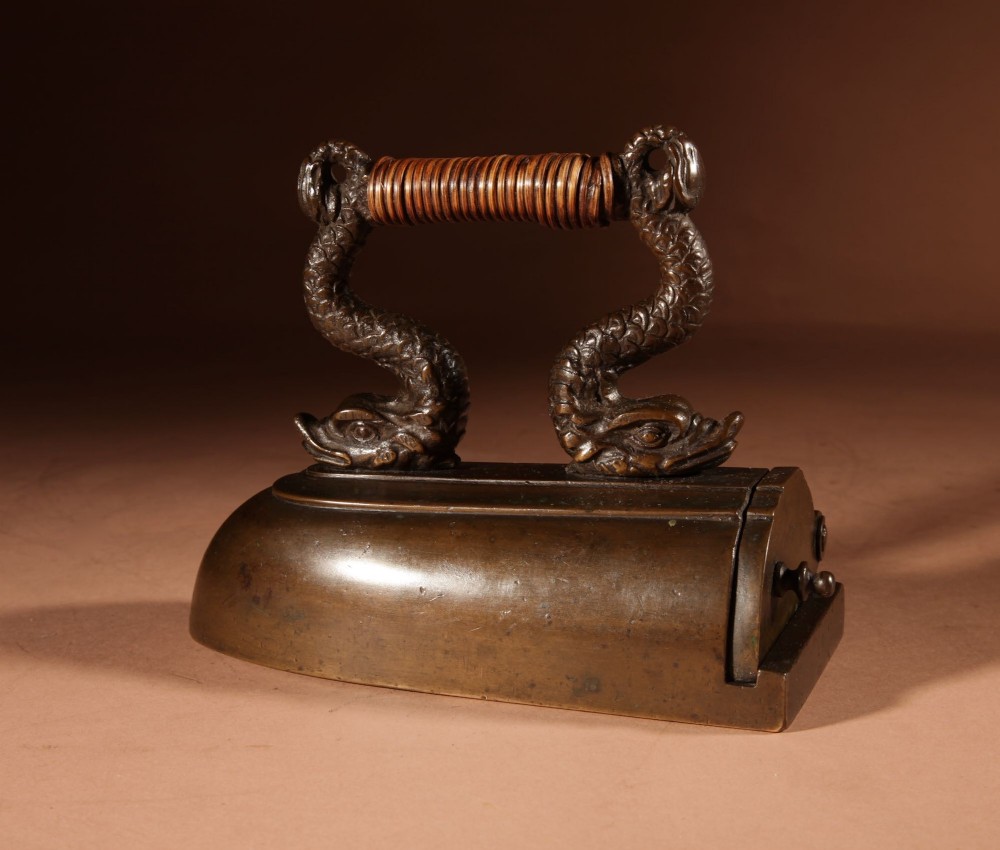 A nineteenth-century French bronze flat iron featuring twin dolphin-shaped supports, a cane-wrapped handle, and a rear door mechanism. View XI